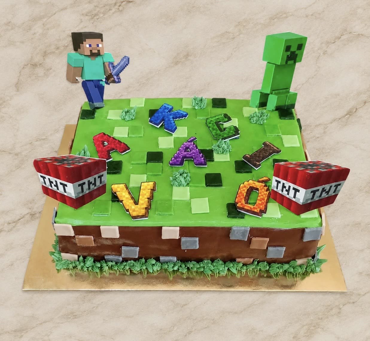 Zöld-barna szögletes Minecraft torta figurákkal és TNT-vel